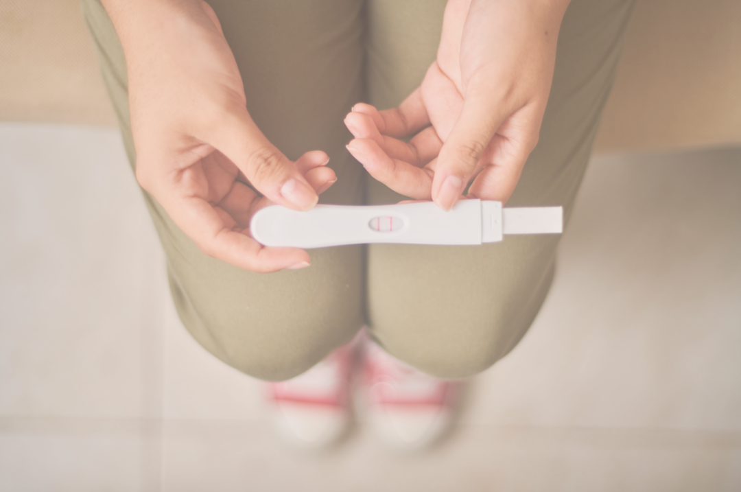 Woman holding a positive pregnancy test while sitting down.